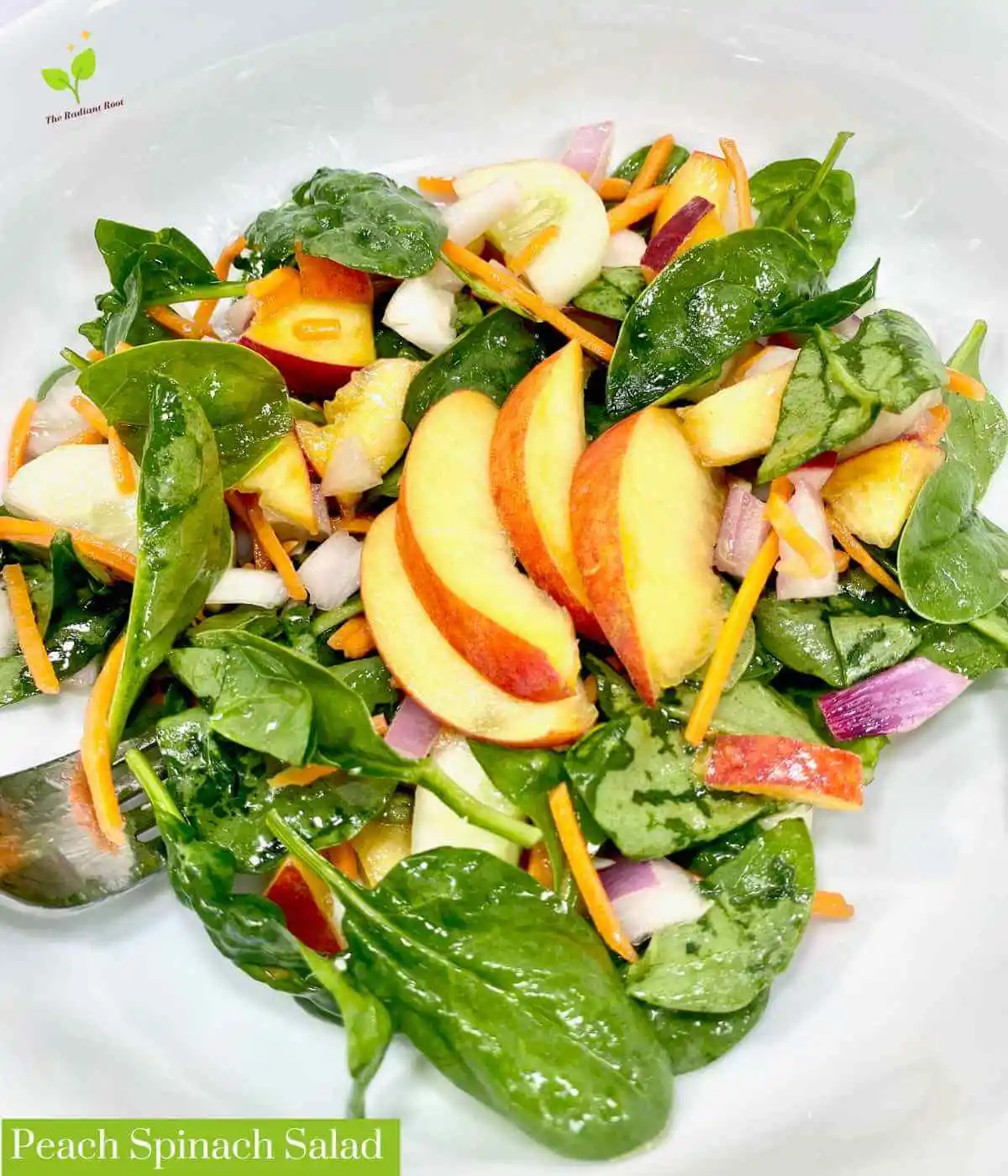 Peach Spinach Salad main photo: A close up of a white marble table containing a large white deep bowl with a finished salad containing peaches, spinach, radishes, cucumber, shredded carrots, and red onion tossed with a red wine vinegar and extra virgin olive oil dressing and topped with sliced peaches as garnish. In the lower left hand corner it reads “Peach Spinach Salad” | salad with peaches | The Radiant Root