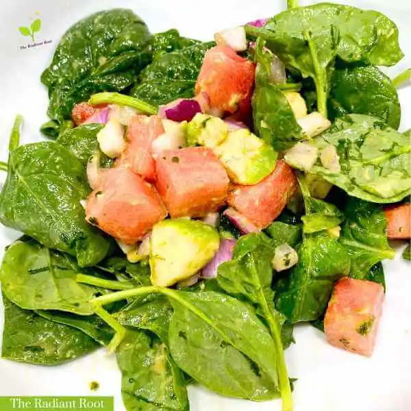 Watermelon avocado salad WP Recipe Photo: A close up of a white large salad bowl with a finished salad containing spinach, watermelon, avocado, and red onion tossed with a dressing containing extra virgin olive oil, cilantro, and lime juice. In the bottom corner it reads “The Radiant Root.” | How to pick a watermelon | The Radiant Root