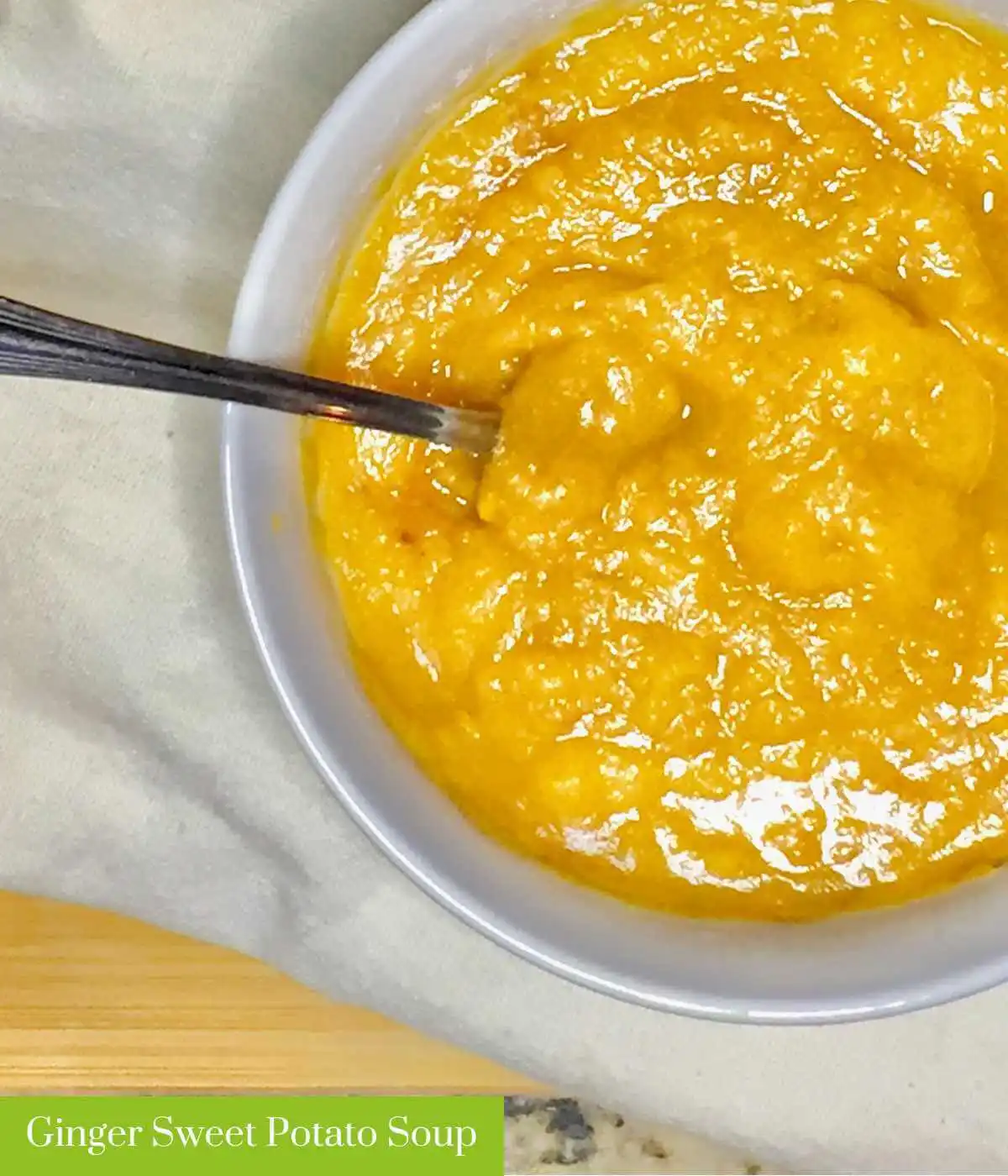 Ginger sweet potato soup in a white bowl with a silver spoon. It reads "Ginger Sweet Potato Soup" in the lower left hand corner | The Radiant Root