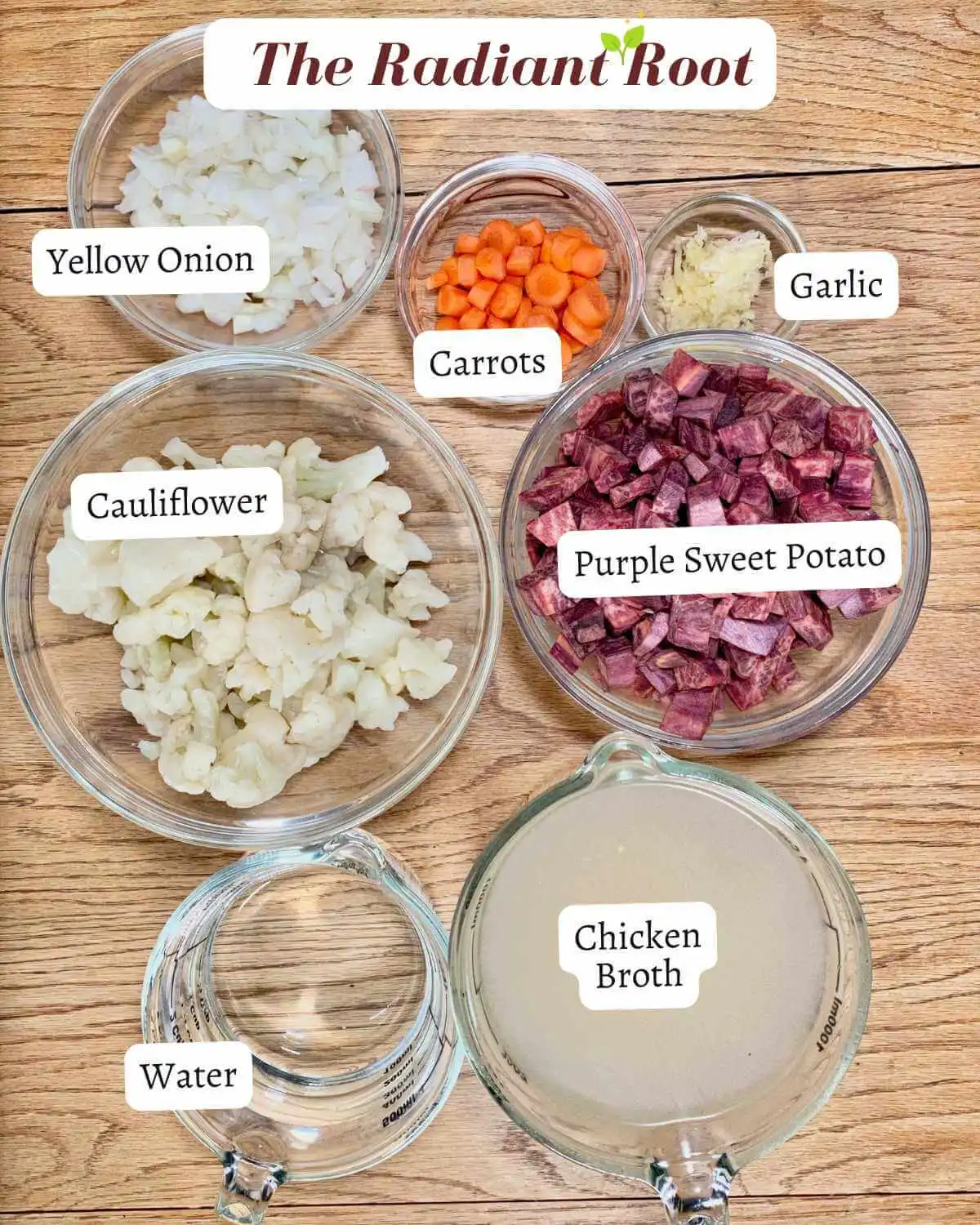 Ingredients for the Purple Sweet Potato Soup on a wooden table in clear glass bowls: yellow onion, raw chopped carrots, fresh pressed garlic, frozen thawed cauliflower, purple sweet potato, filtered water, chicken broth | Purple Sweet Potato Soup | The Radiant Root